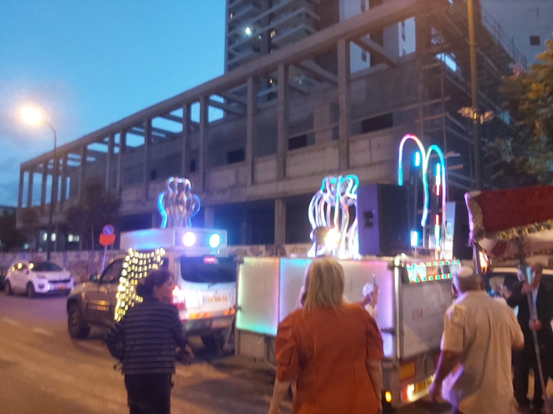 An illuminated vehicle leading an evening street procession in Tel Aviv